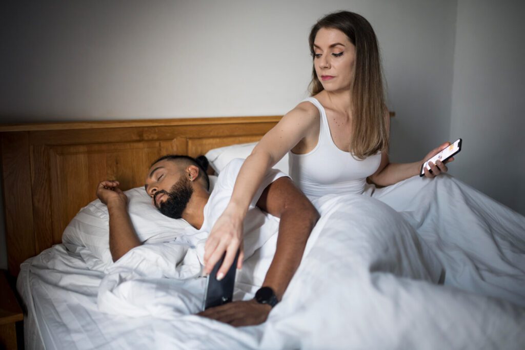 mujer comprobando el teléfono de su novio mientras duerme